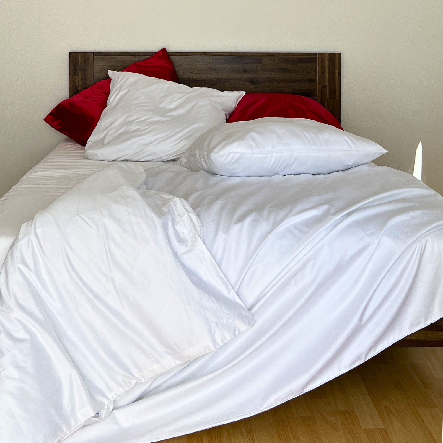 Weißes Bett mit roten Kissen und einem weißen, handgefertigten Bettbezug aus ägyptischer Baumwolle